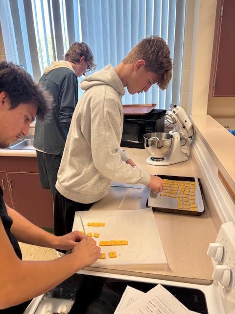 A student cutting out squares to put on the baking sheet