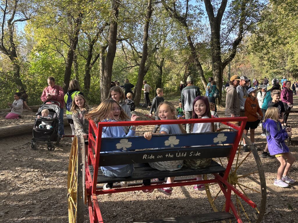 Three girls riding in a buggy while two girls try to pull them.