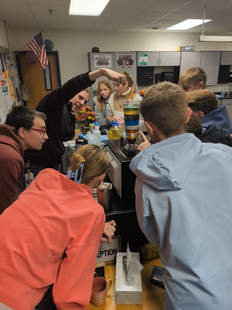 A teacher dropping an object into the container with the different liquids while the students watch.