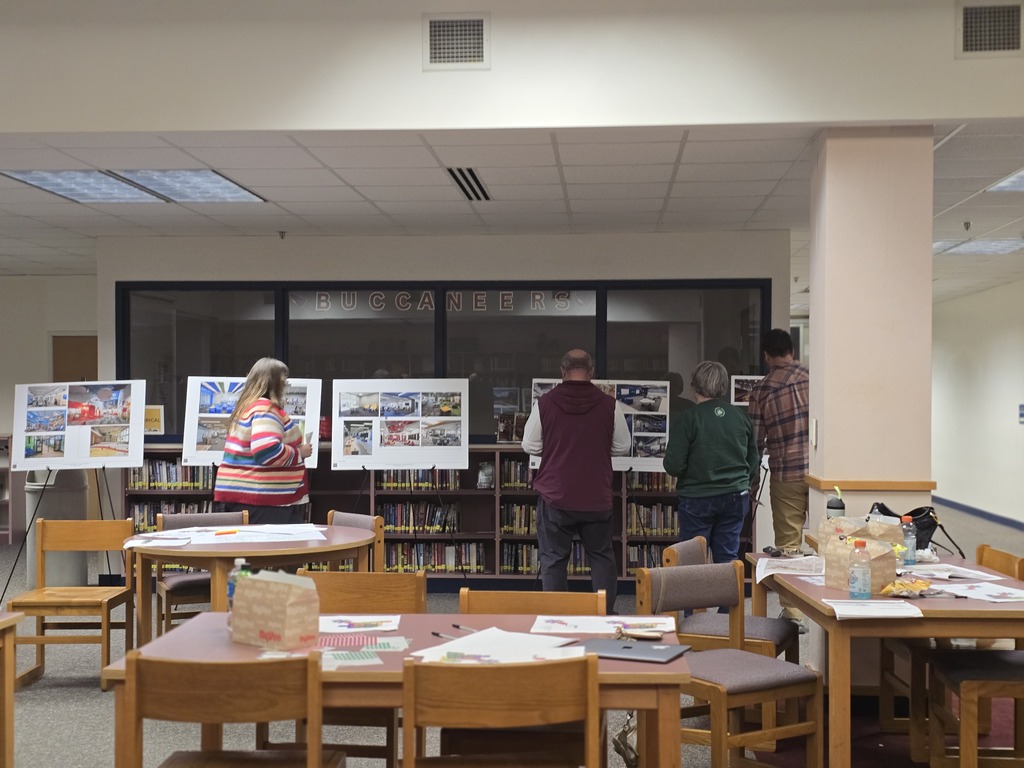 Four people examining posters on easels in a library; books on shelves behind them.