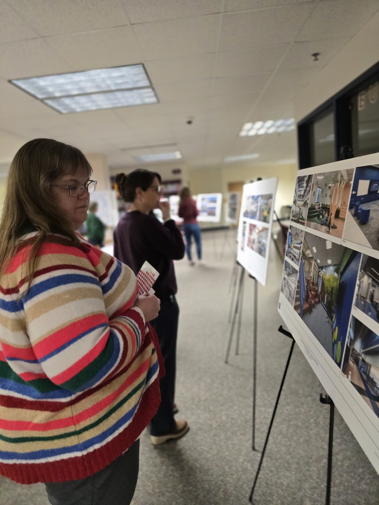 A woman examines photographs displayed on an easel. A second woman views photographs in the background.