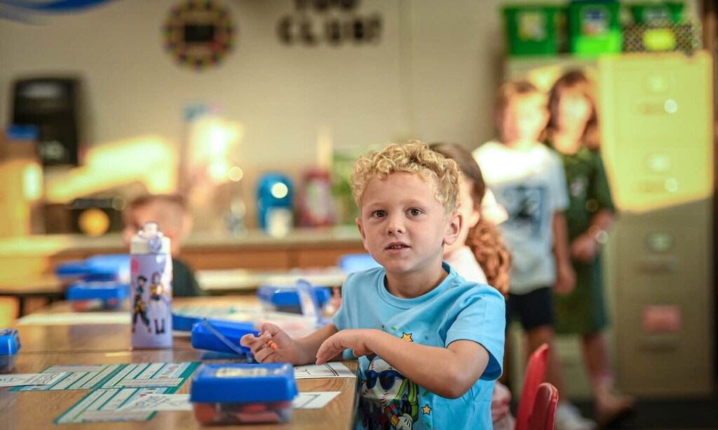 A boy in a blue shirt sits at a table.