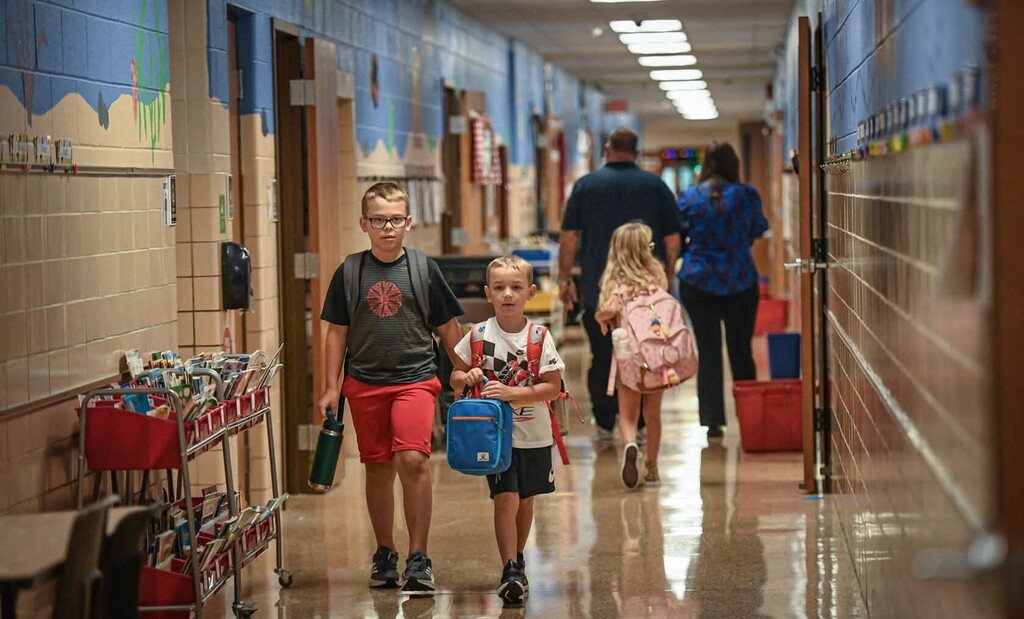 Children walking down a school hallway, carrying backpacks.