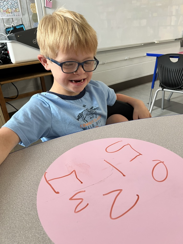 Writing numbers independently with a dry erase marker. 