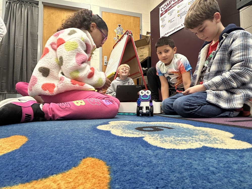 four students with LEGO sitting on rug