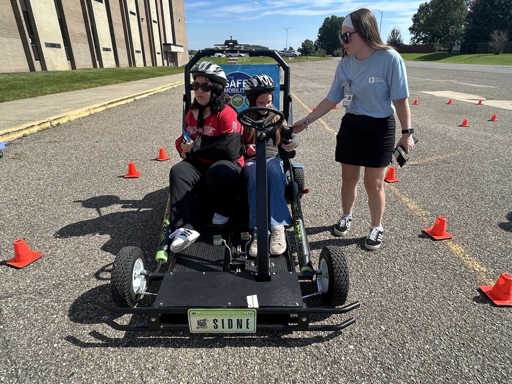two students in a go cart with akron children's worker buckling them up to run a course