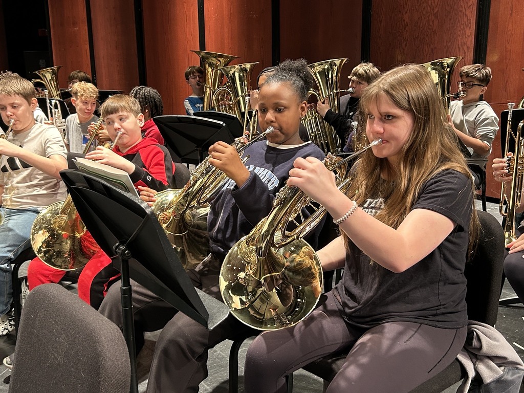 two girls in the forefront playing their horns with tubas behind them