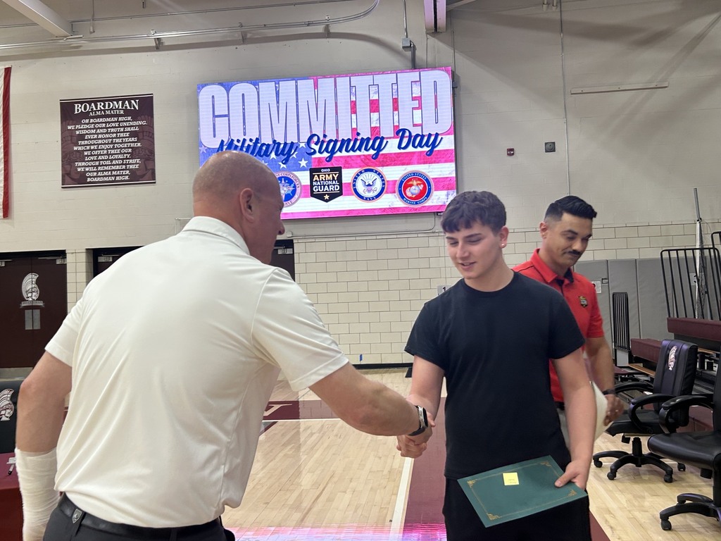 Principal Zura shaking Jeffery Heidel's hand with military signing day sign