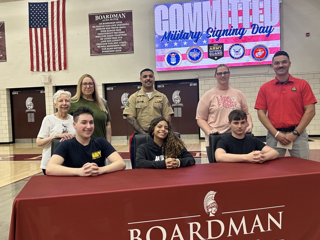 3 students sitting at table with family and recruiters behind them in gymnasium