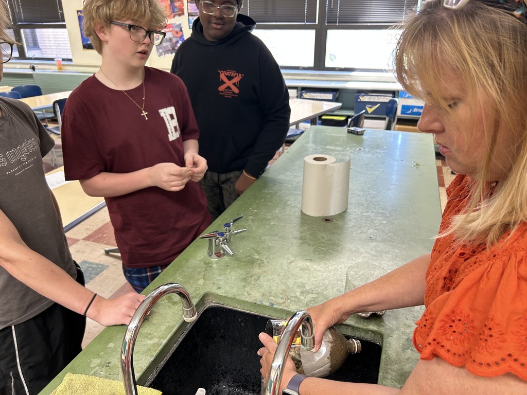 Mrs. Neifer helps 3 students restart their water filtration experiment 