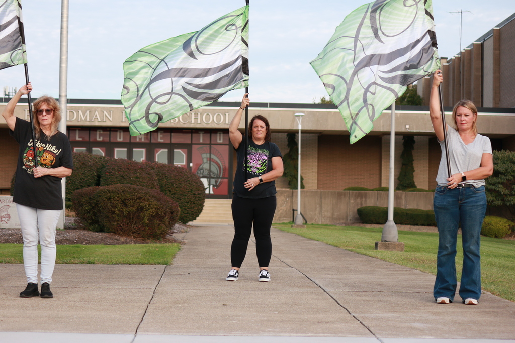 alumni with 3 flags in green and black practicing moves in front of the high school