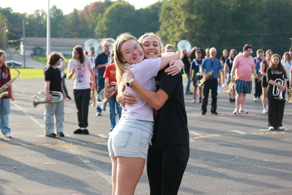alumni and current student hugging with band practicing on the parking lot behind them