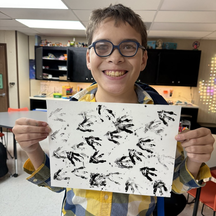 Student in blue glasses smiles and holds a print artwork featuring dinosaur footprints 