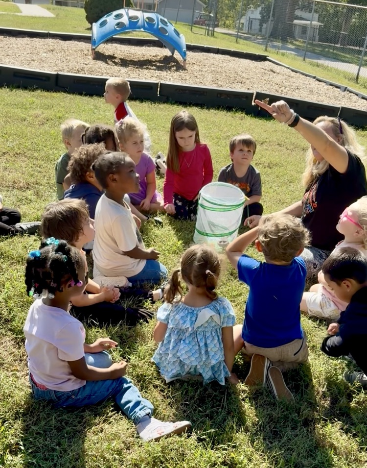 Miss Maria has a butterfly on her finger and the Green Room kids look on.