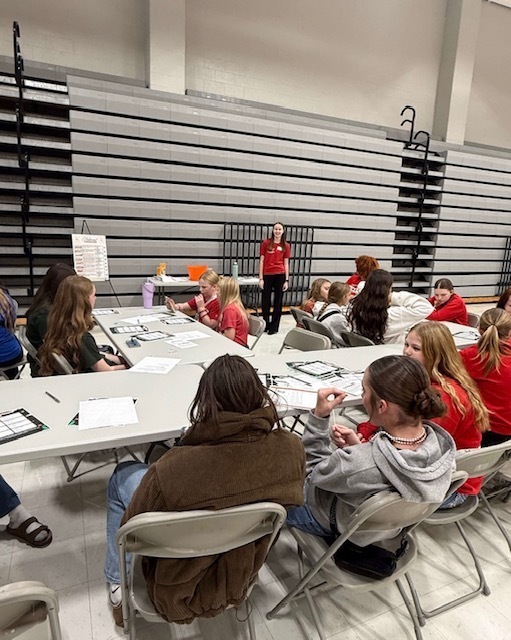 Students sit at tables participating in an FCCLA workshop inside the gym while a student leader presents at the front of the room.