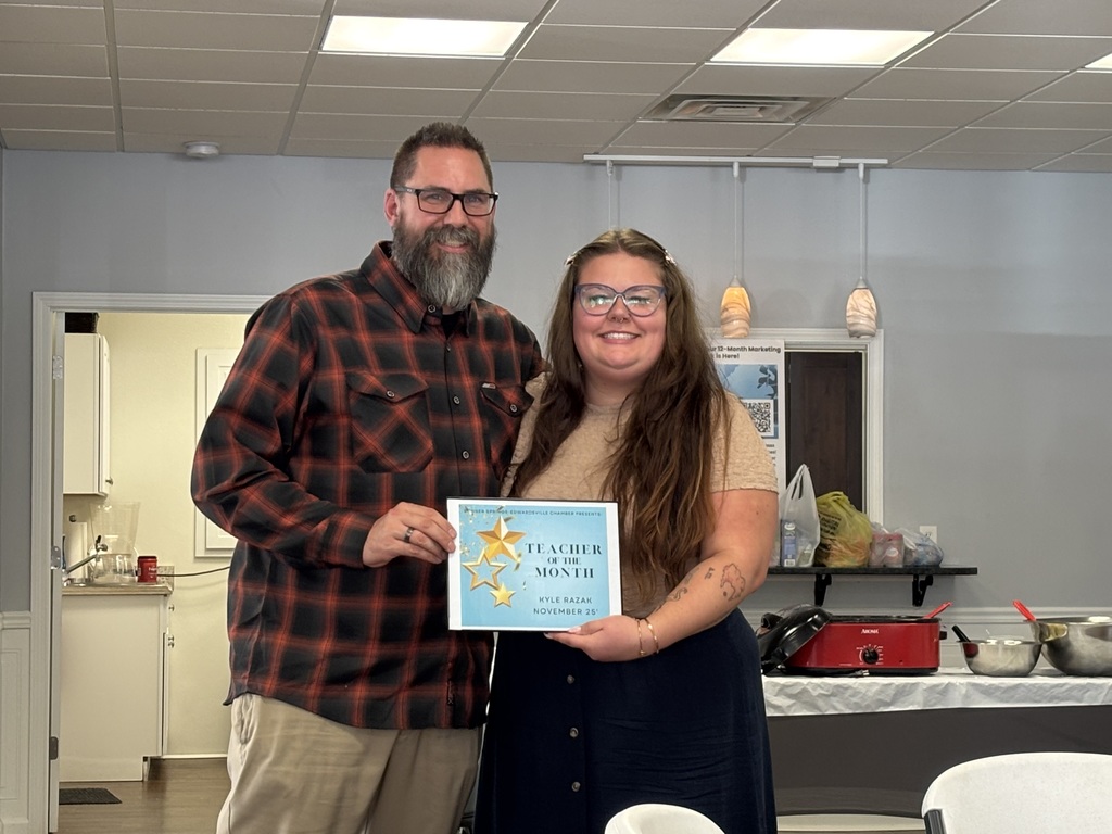 Kyle Razak, math teacher at Clark Middle School and head track and field coach at Bonner Springs High School, stands smiling beside another individual while holding his November Teacher of the Month certificate at a Bonner Springs/Edwardsville Chamber of Commerce luncheon.