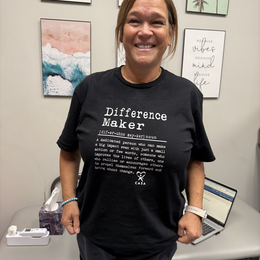 Nurse Kim smiling while wearing a black T-shirt that reads “Difference Maker” with a definition below it describing a dedicated person who makes a big impact through their actions and words. The shirt also includes the CASA logo at the bottom.