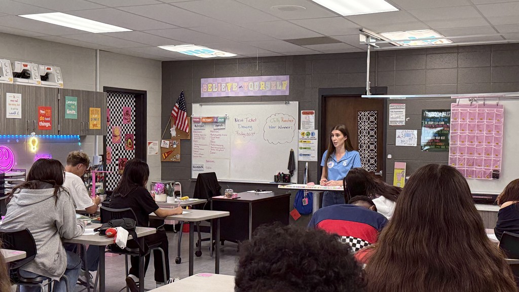 Meteorologist Stevie Stephenson from KCTV5 News speaks to Career and Life Planning students at Clark Middle School about her work in broadcast meteorology. Students are seated at desks listening attentively in a classroom decorated with motivational posters and an American flag.