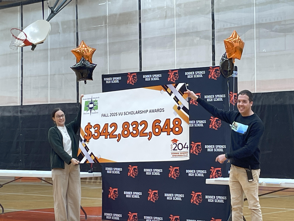 Two adults stand in a high school gym holding a large banner that reads “Fall 2025 VU Scholarship Awards: $342,832,648.” They are smiling, with orange and black star-shaped balloons behind them and a Bonner Springs High School backdrop in the background.