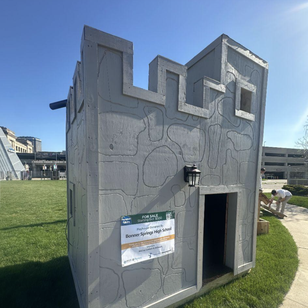Small, concrete structure resembling a castle with an open door. Green sign on wall. Person nearby.