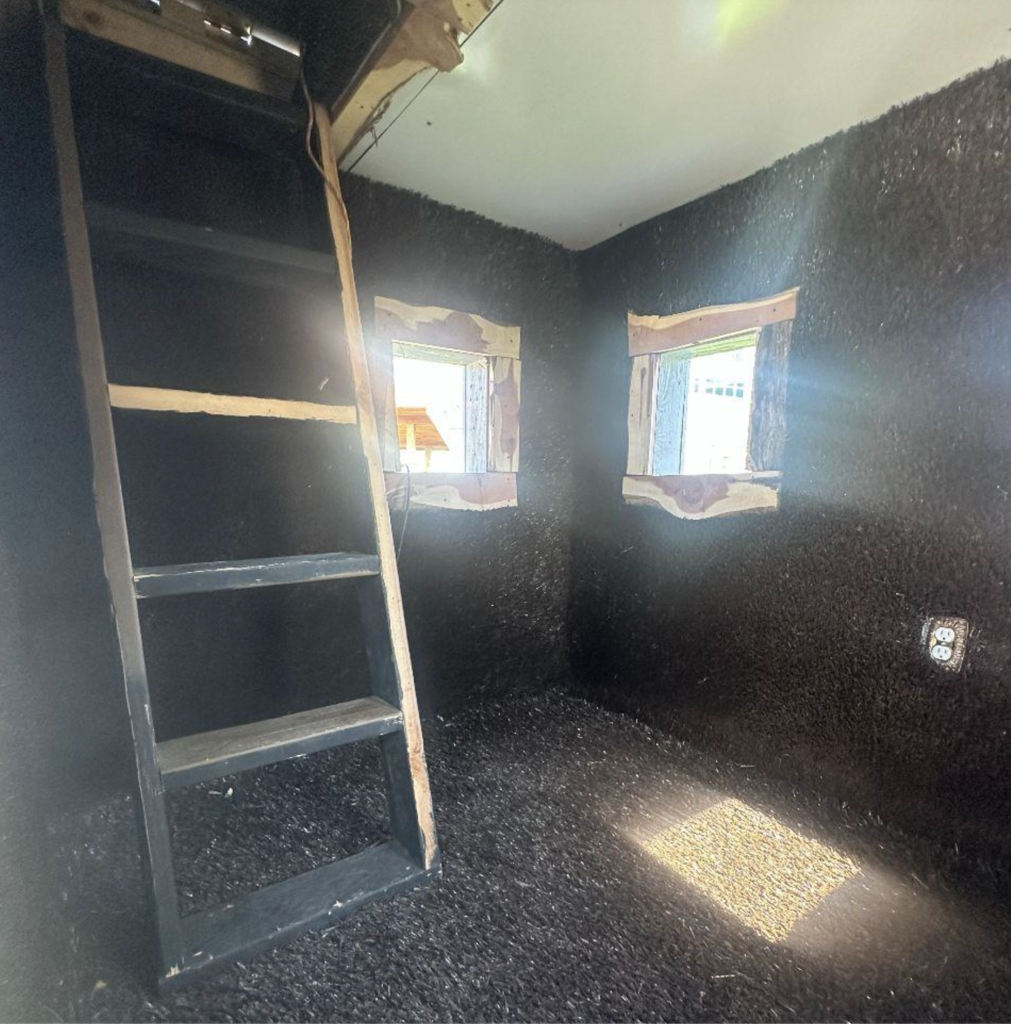 A dark room with two small windows. An unfinished wall is visible, with a ladder leaning against it.