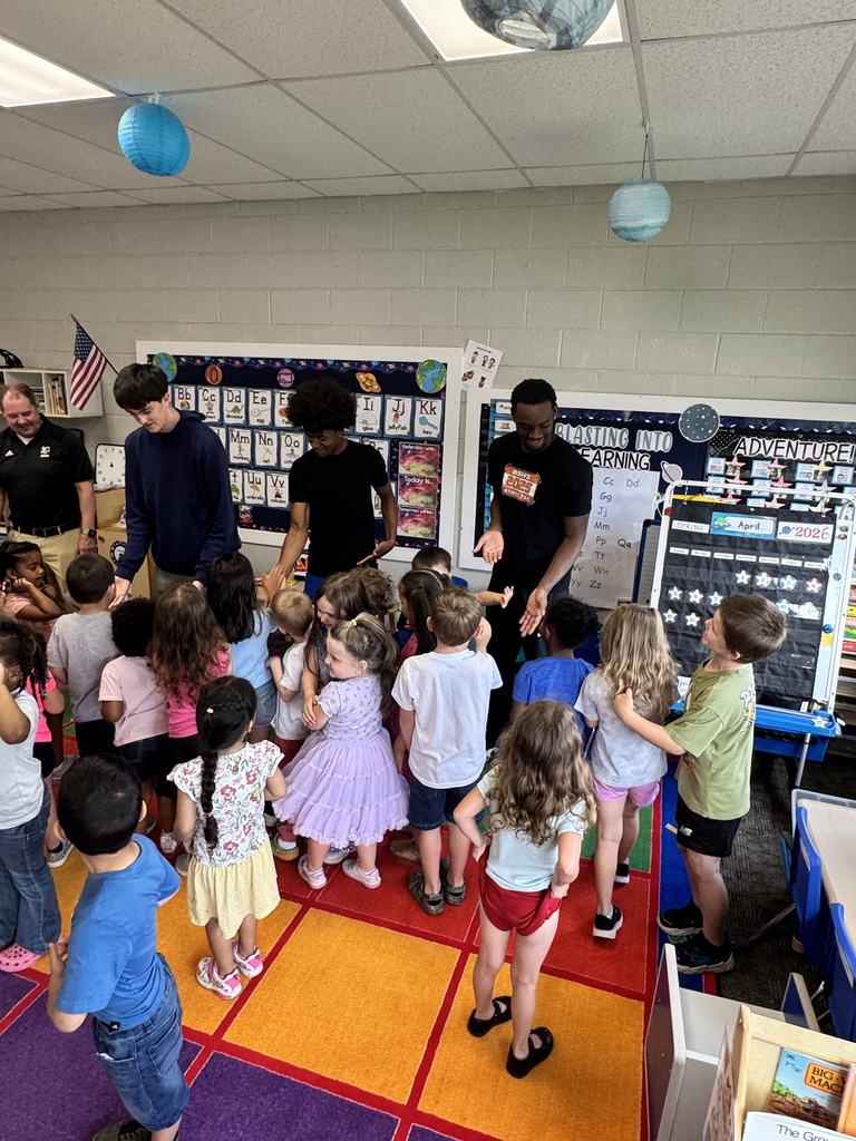 A group of children in a classroom with teachers; one teacher holds a child's hand.