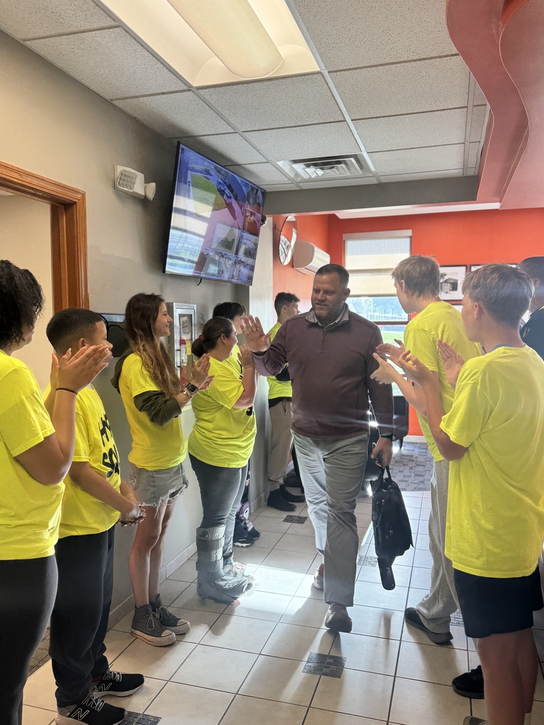 Several people in yellow shirts clapping for a man in a hallway. 