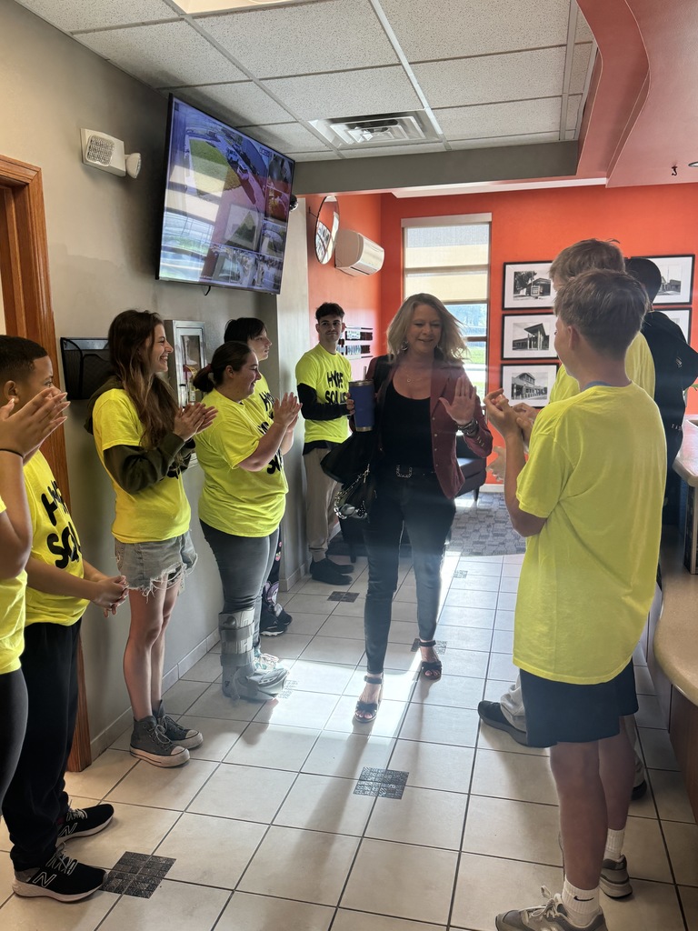 A group of people in yellow shirts stand in a hallway. A woman stands in the middle.