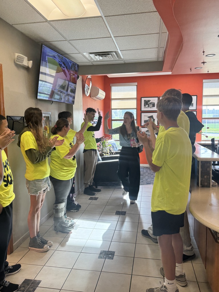 Group of people in yellow shirts stand in a hallway; one person walks near a counter.