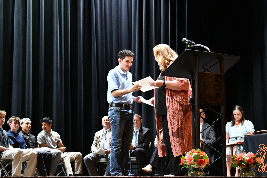 A man stands at a podium receiving an award from a woman. People are seated in the audience.