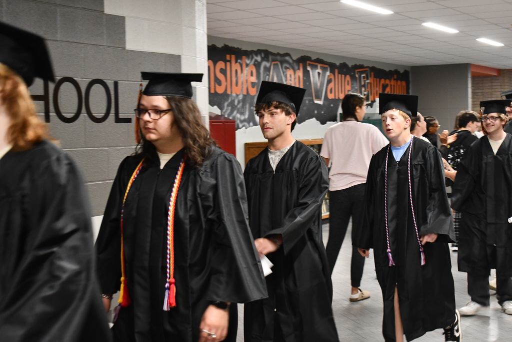 A group of people in graduation gowns walk down a hallway with graffiti on a wall.