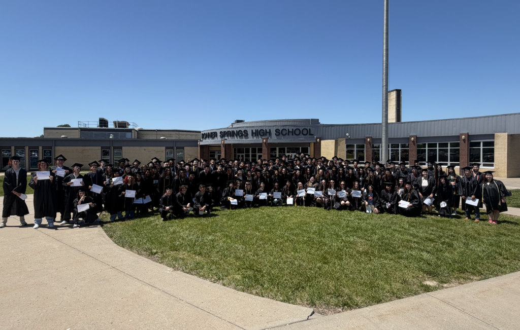 A group of people in graduation attire pose for a photo in front of Bonner Springs High School.