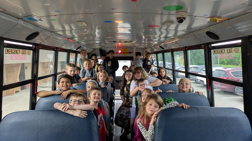 A school bus filled with children seated on blue seats, with some leaning on the windows.