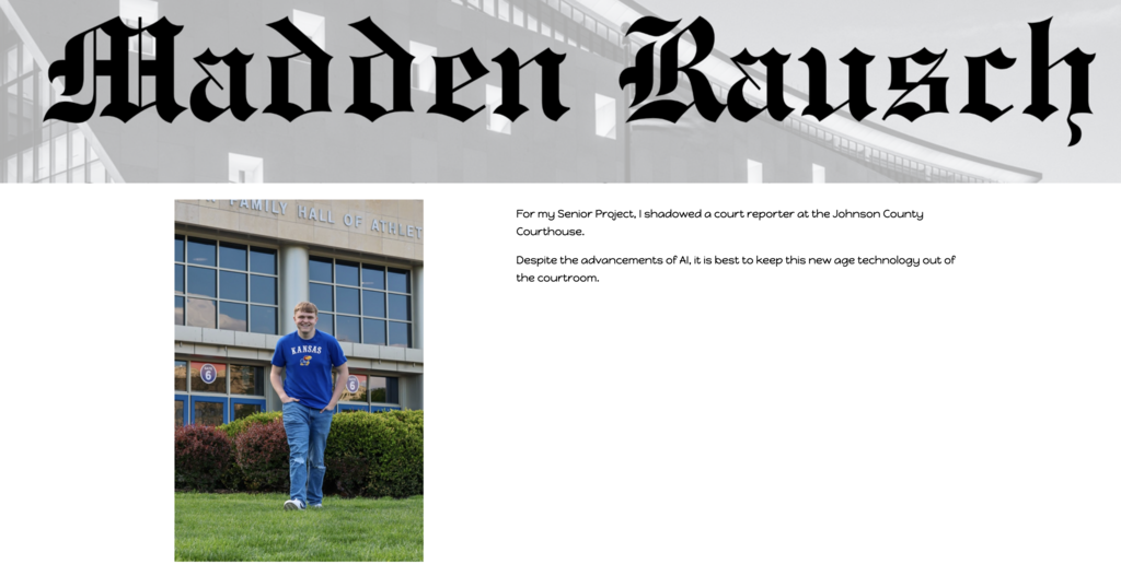 A man in a blue shirt and blue jeans stands on grass before a school building.