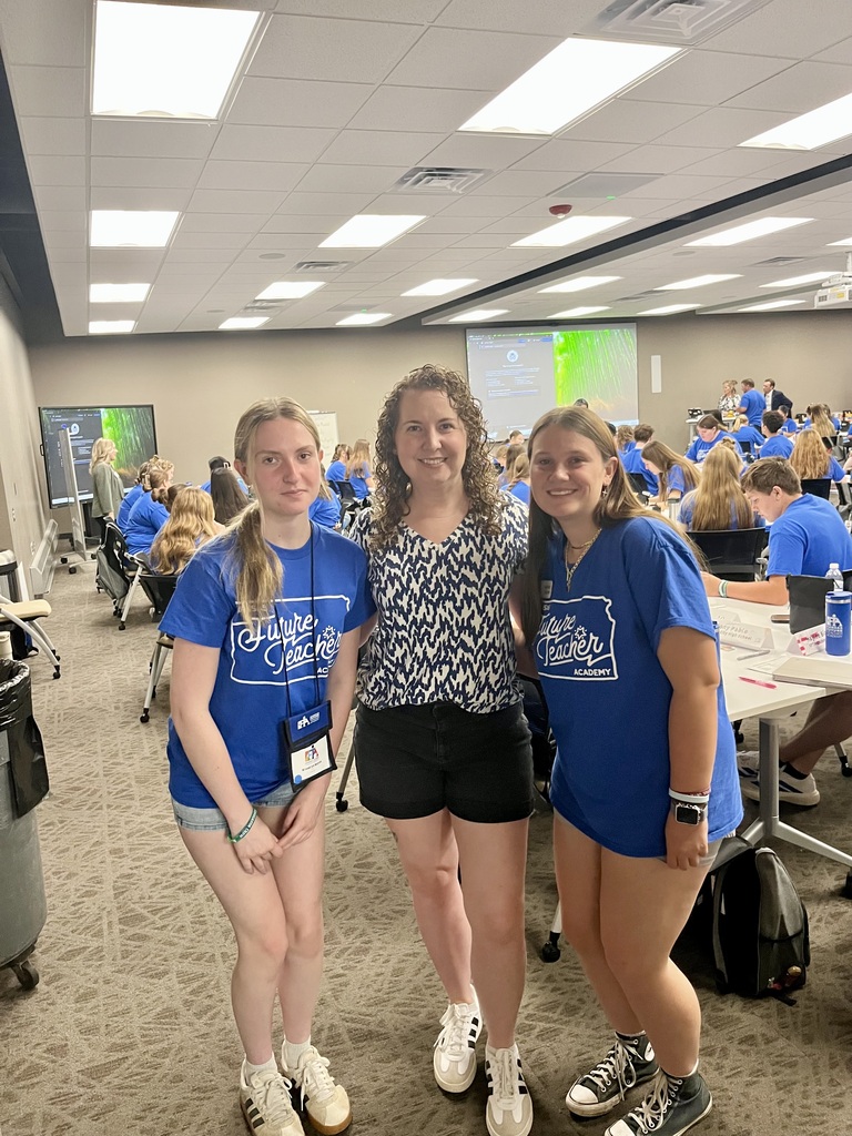 Three people in blue shirts and shorts pose for a photo in a room with tables and chairs.