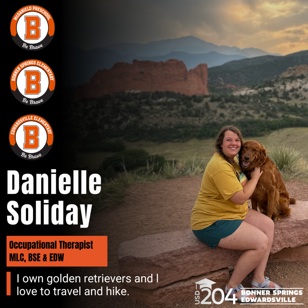 A woman sits on a rock with a golden retriever, both smiling, in front of a sunset and mountains.