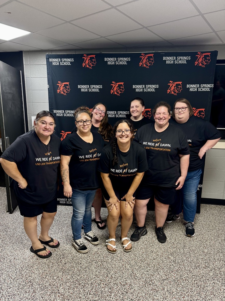 Group of people in black t-shirts posing for a photo in front of a school banner.
