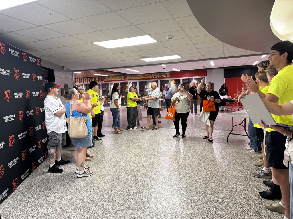 A group of people wearing yellow shirts and other colors stand in line in a hallway.