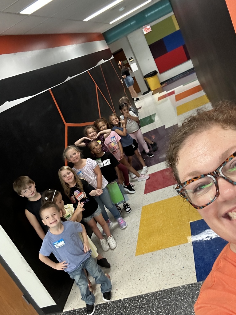 A group of children standing in a colorful hallway with a smiling adult in front of them.