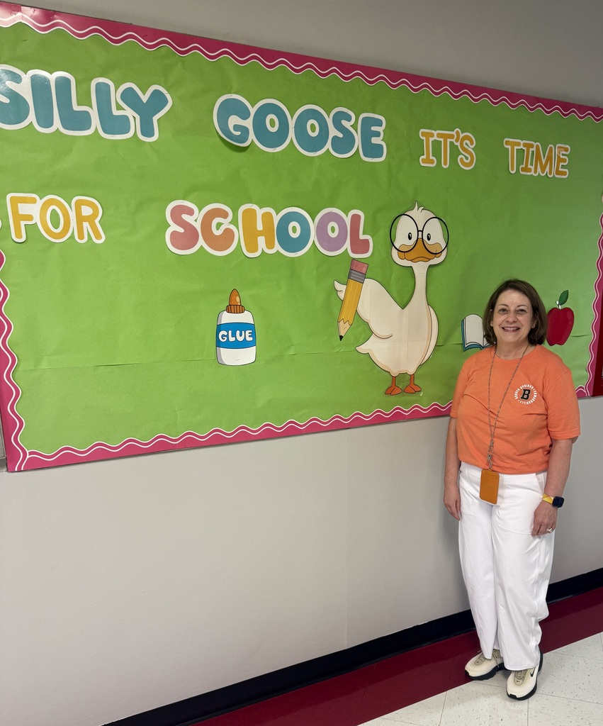 A woman stands before a green banner with pink trim, featuring a goose, a pencil, and text.