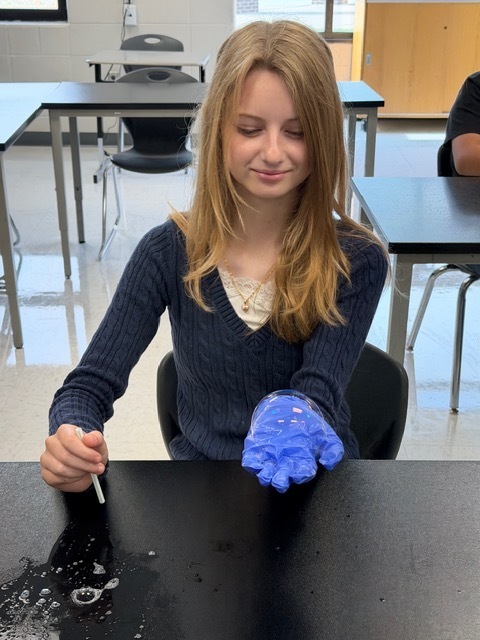 A student in a classroom is using a dropper to pour a substance on a table.