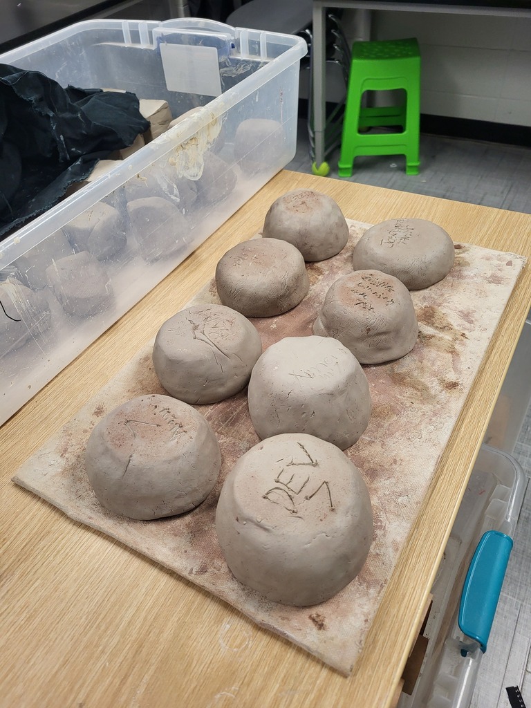 Round clay pieces are on a table. One reads "REV". There is a clear container holding objects nearby.