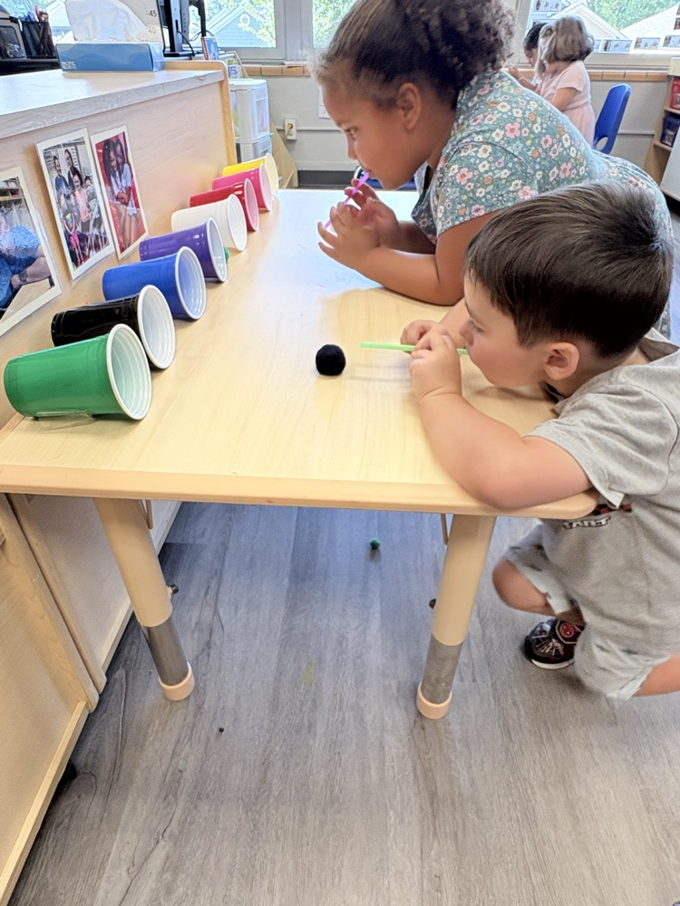 learning activities and motor skills. kids blow a puff ball in to a cup with a straw.