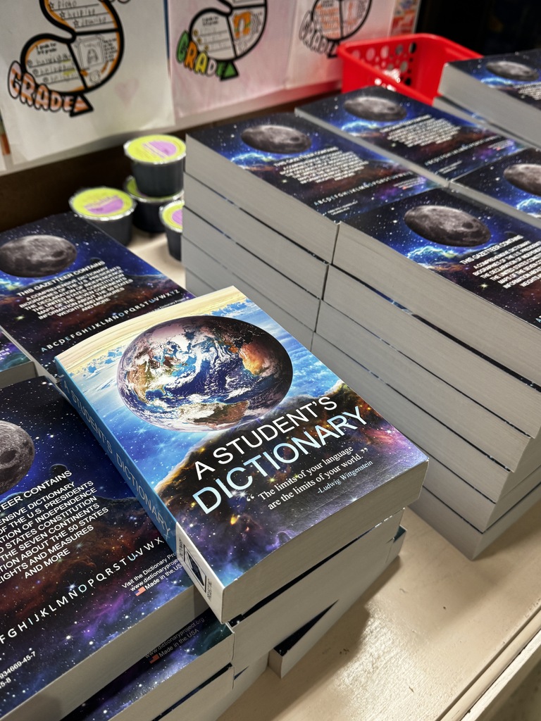 Books titled "A Student's Dictionary" with space and planet visuals on covers. Some books in stacks, others on a table.