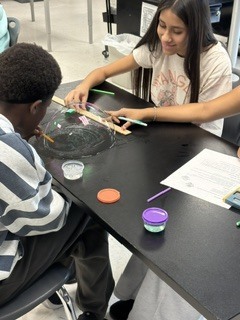 A student works on a science project at a table with a bowl and a paper.