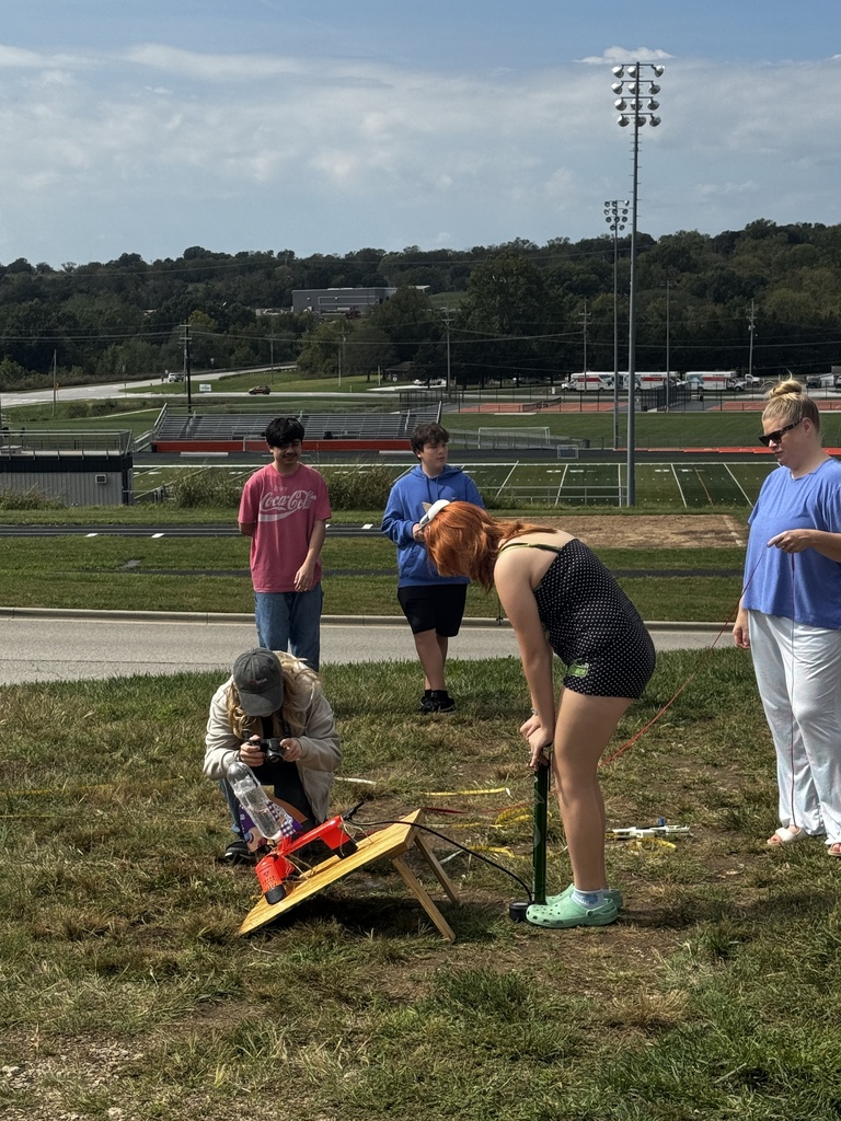 Five people on a field with a grassy surface. One woman leans over a small yellow platform.