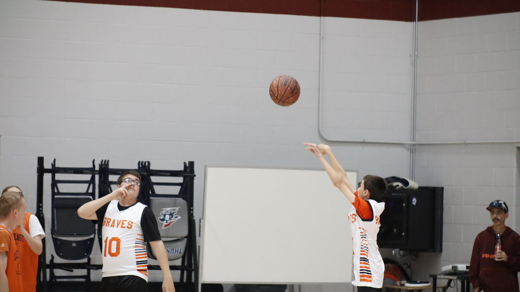 Two individuals play basketball indoors. One player throws the ball, while another reaches for it.