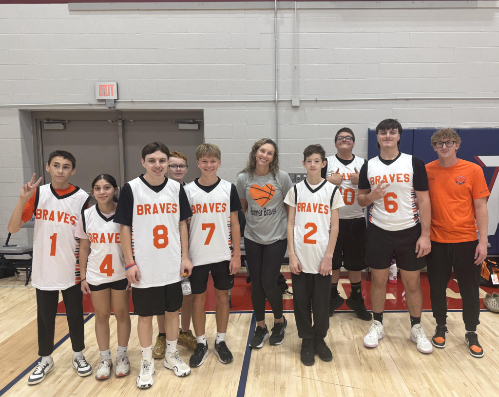 Group of young basketball players standing on a basketball court. Some wear jerseys with numbers.