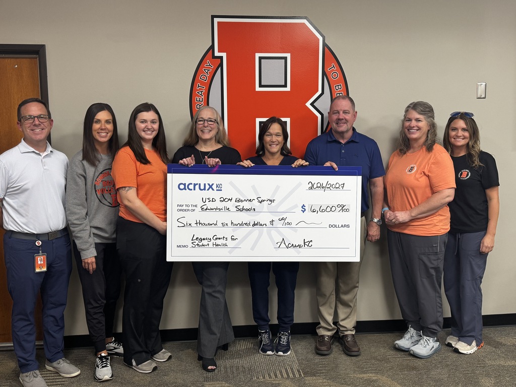 A group of adults holding a large check in front of a wall with a large red letter "B".