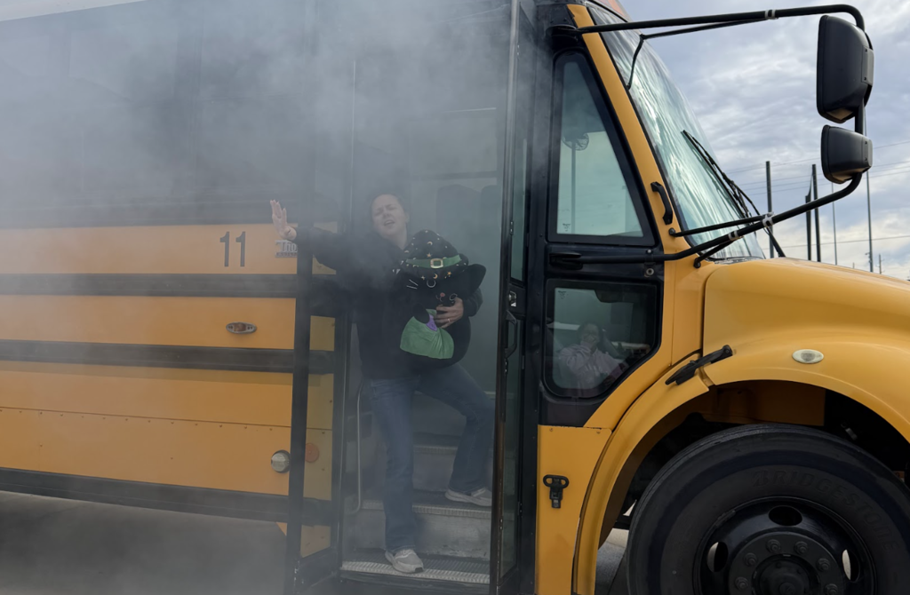 A person stands on the steps of a yellow school bus, holding a green bag, with smoke in the air.